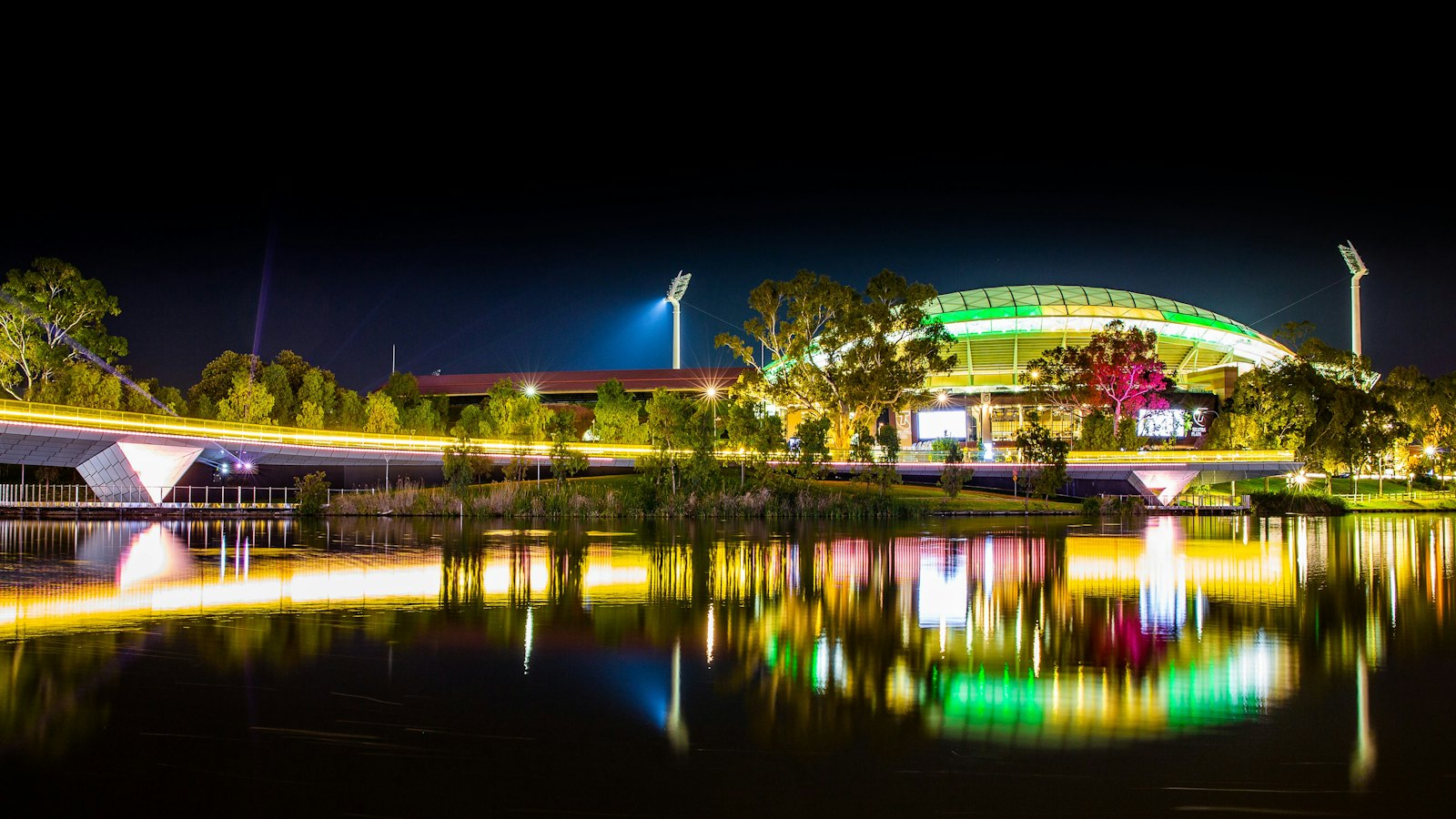Adelaide Oval glowing green and gold beside the River Torrens footbridge at night