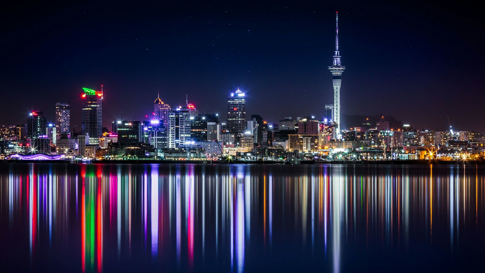 Auckland skyline and the Sky Tower at night, city lights reflected across the Waitemata Harbour