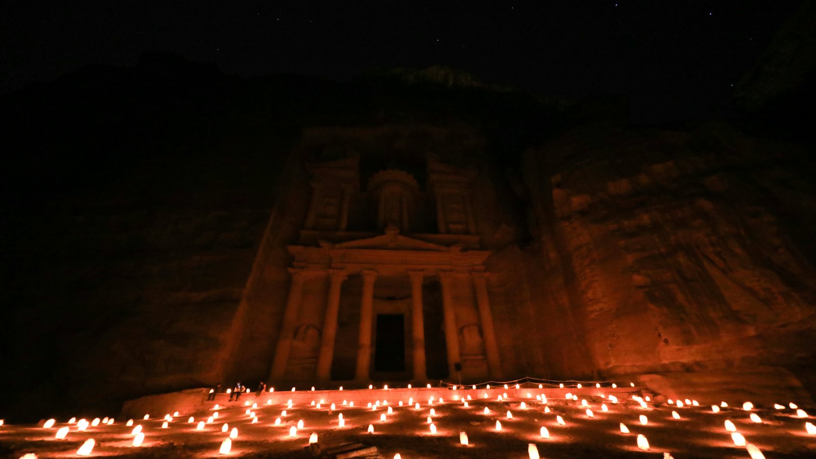 Ancient Treasury facade at Petra glowing above rows of lit candles at night