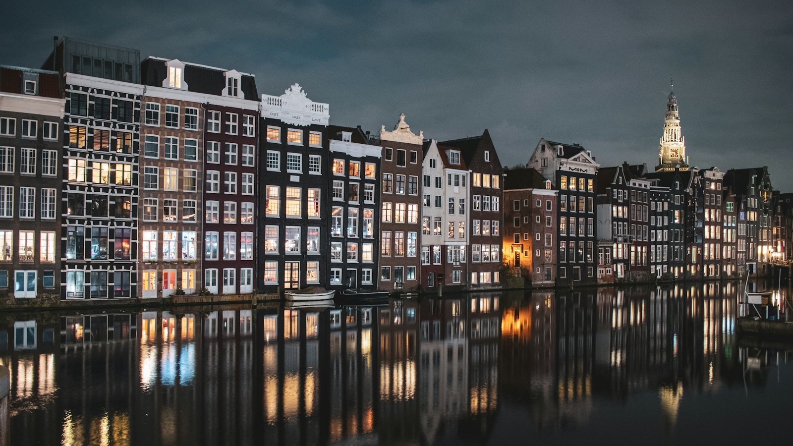 Illuminated Damrak canal houses and the Oude Kerk tower reflected in Amsterdam water at night
