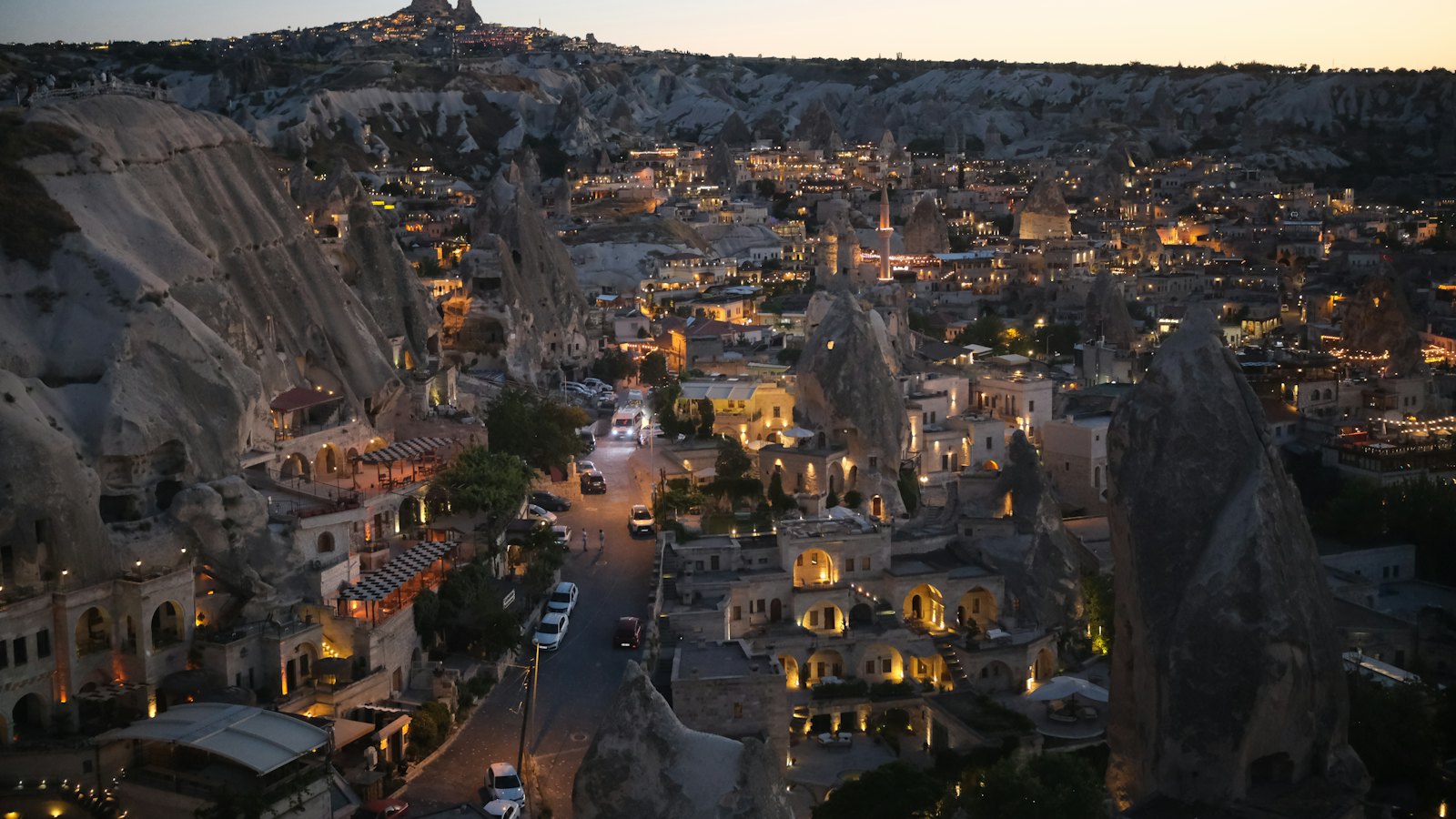 Fairy chimney cave village glowing at dusk beneath a rocky hilltop in Cappadocia