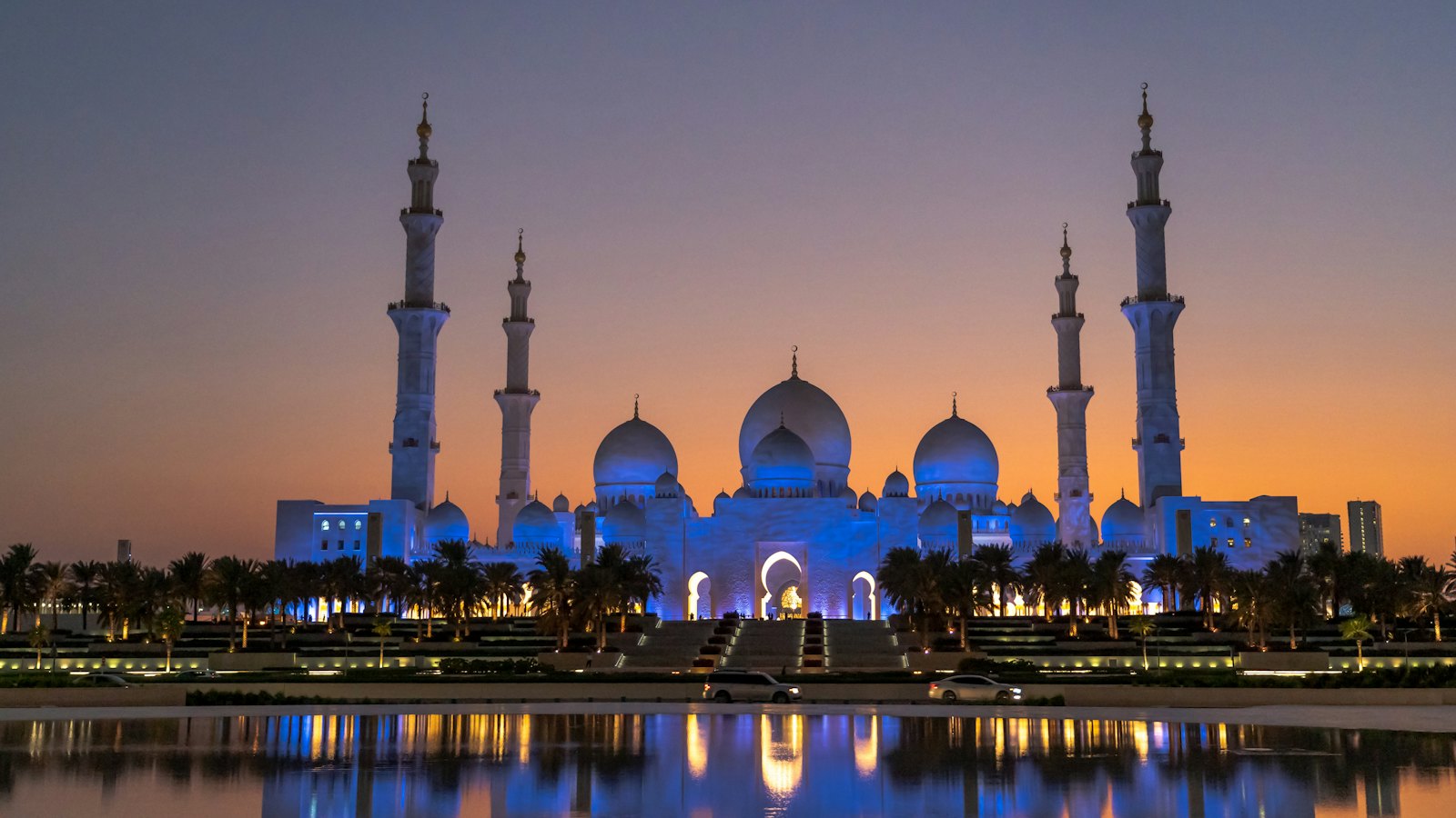 Sheikh Zayed Grand Mosque in Abu Dhabi at dusk, lit blue above its reflecting pool