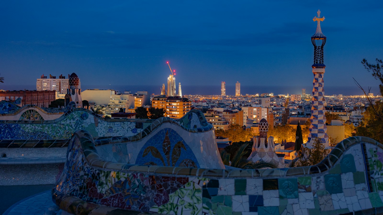 Park Güell mosaic bench and gatehouse tower overlooking Barcelona and the Sagrada Família at blue hour