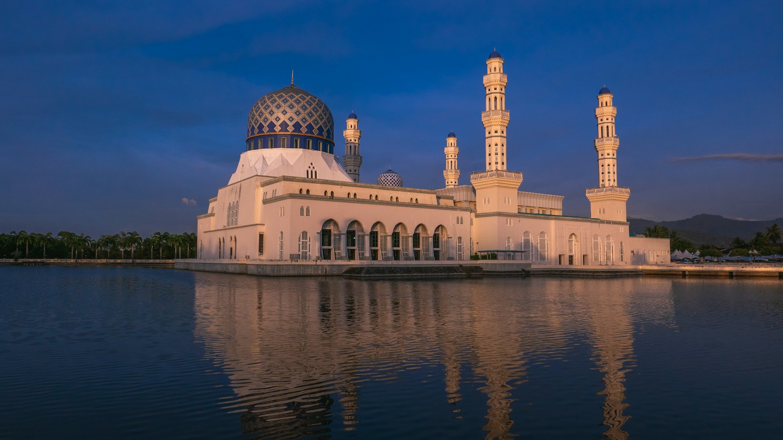 Kota Kinabalu City Mosque glowing at dusk, reflected in its lagoon under a deep blue sky