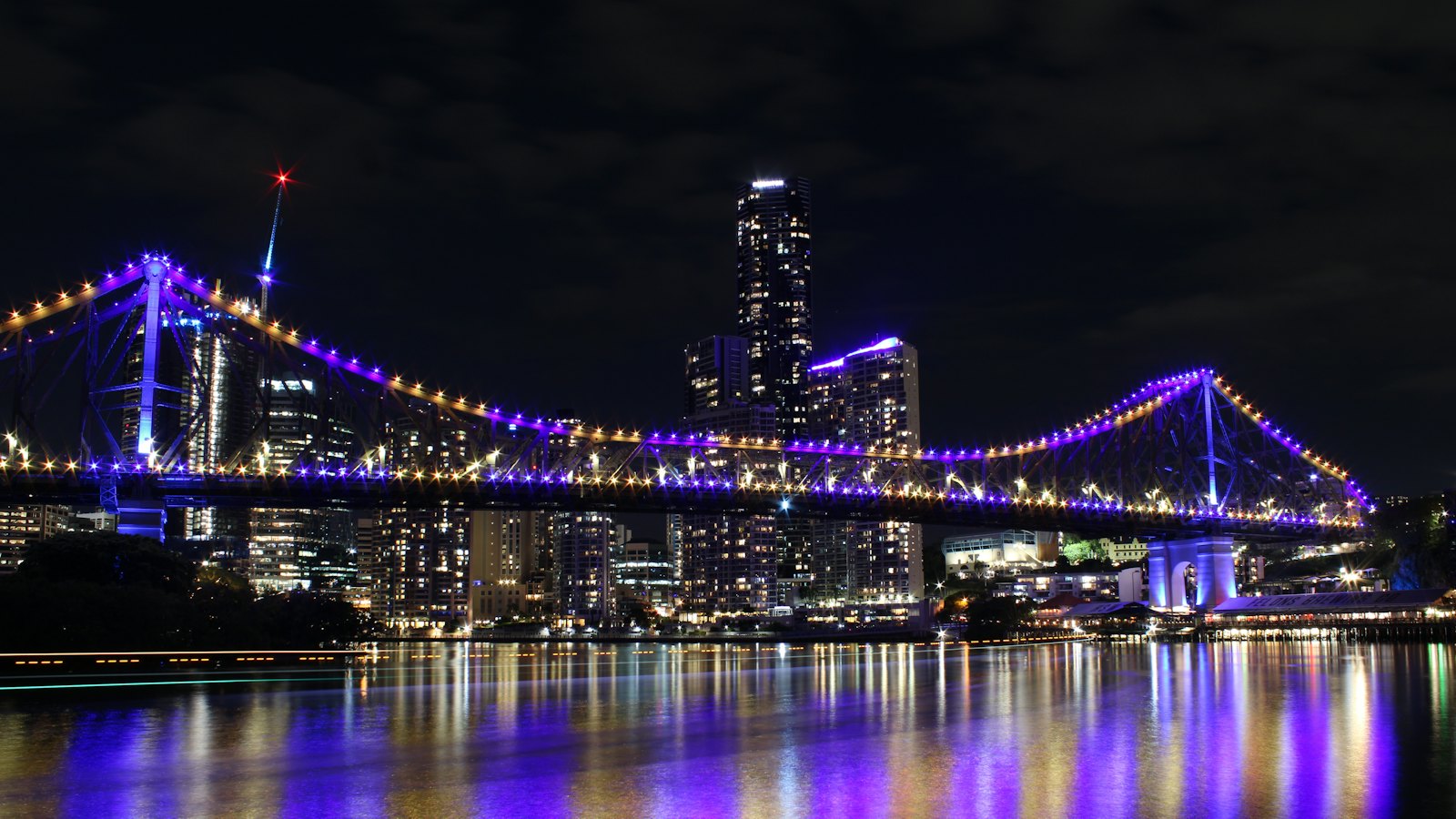 Story Bridge lit purple at night over the Brisbane River, city towers behind