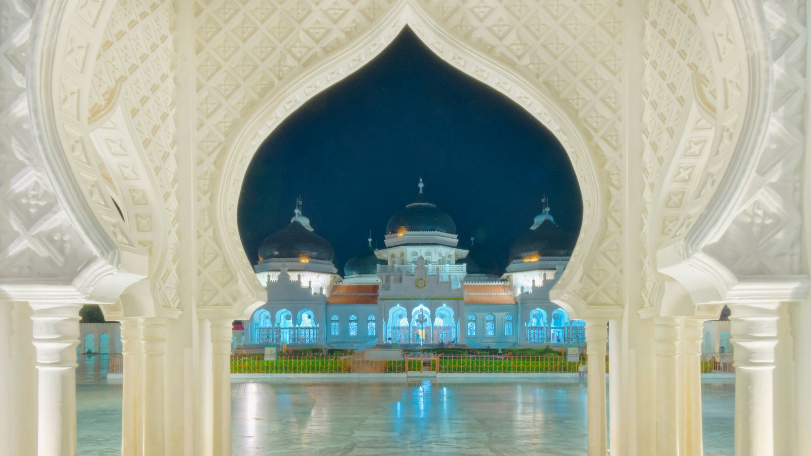 Baiturrahman Grand Mosque illuminated at night, framed by an ornate archway in Banda Aceh
