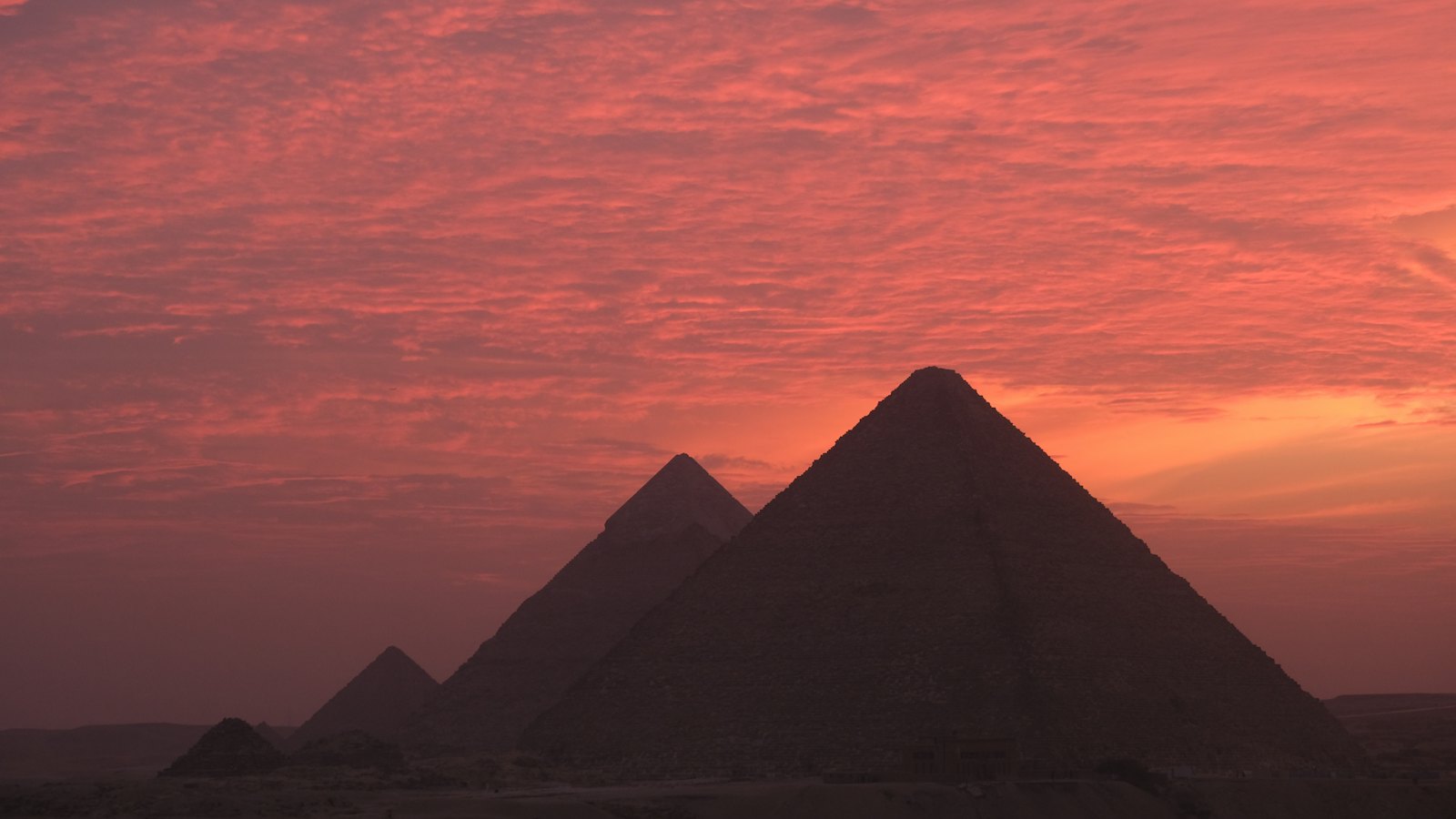 Silhouetted Great Pyramids of Giza under a glowing pink sunset sky near Cairo, Egypt
