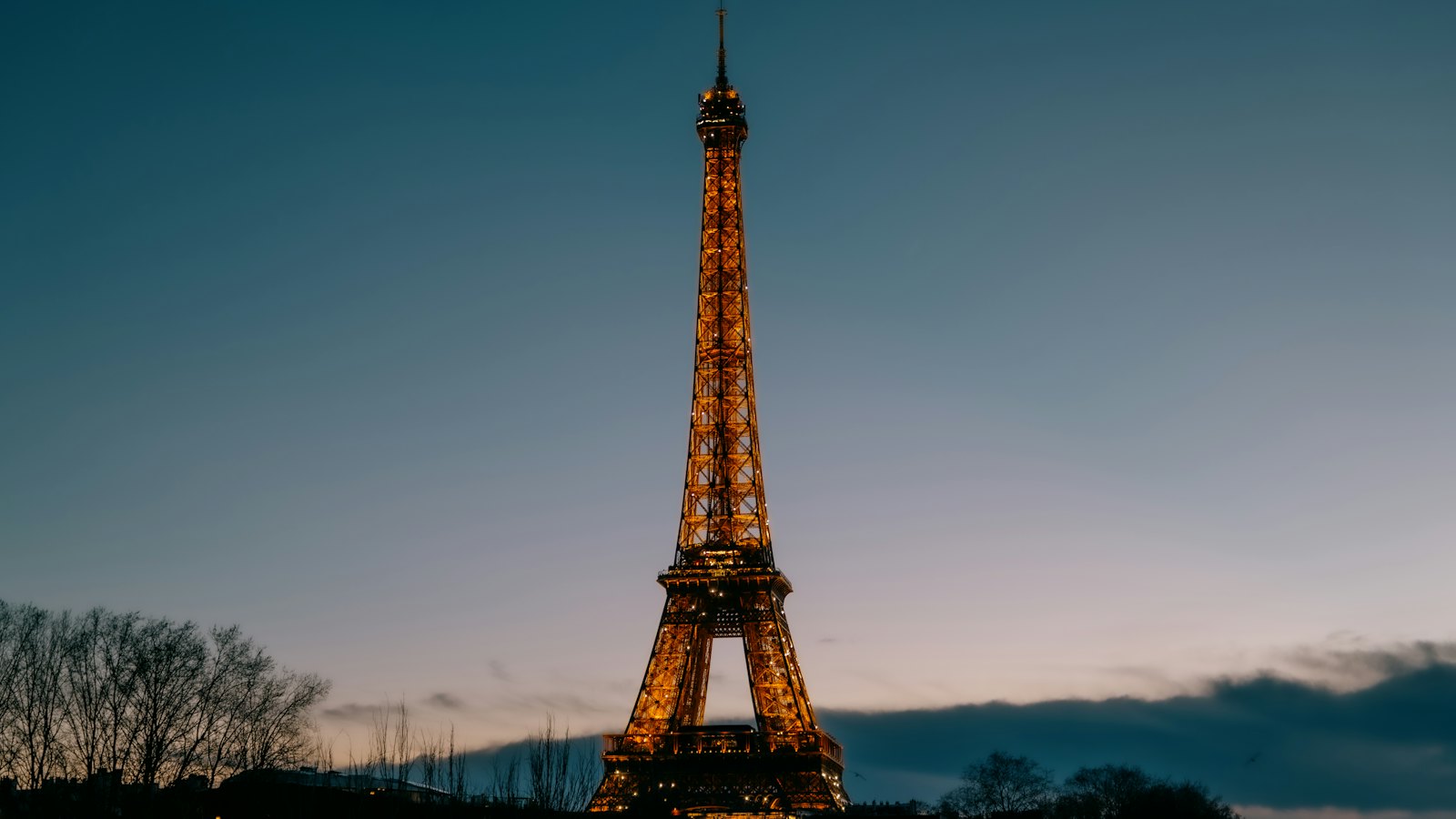 The Eiffel Tower lit gold at dusk against a deep blue sky in Paris