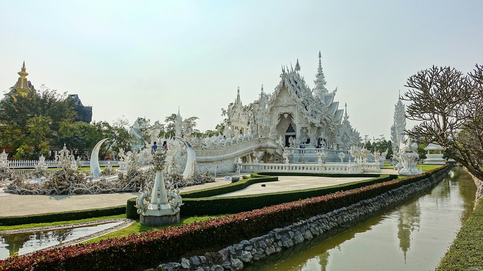 Wat Rong Khun's ornate white spires reflected near a pond in Chiang Rai