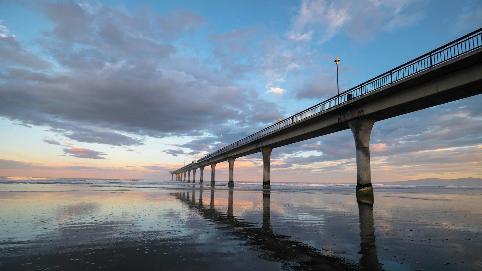 New Brighton Pier stretching over the wet sand at dusk near Christchurch
