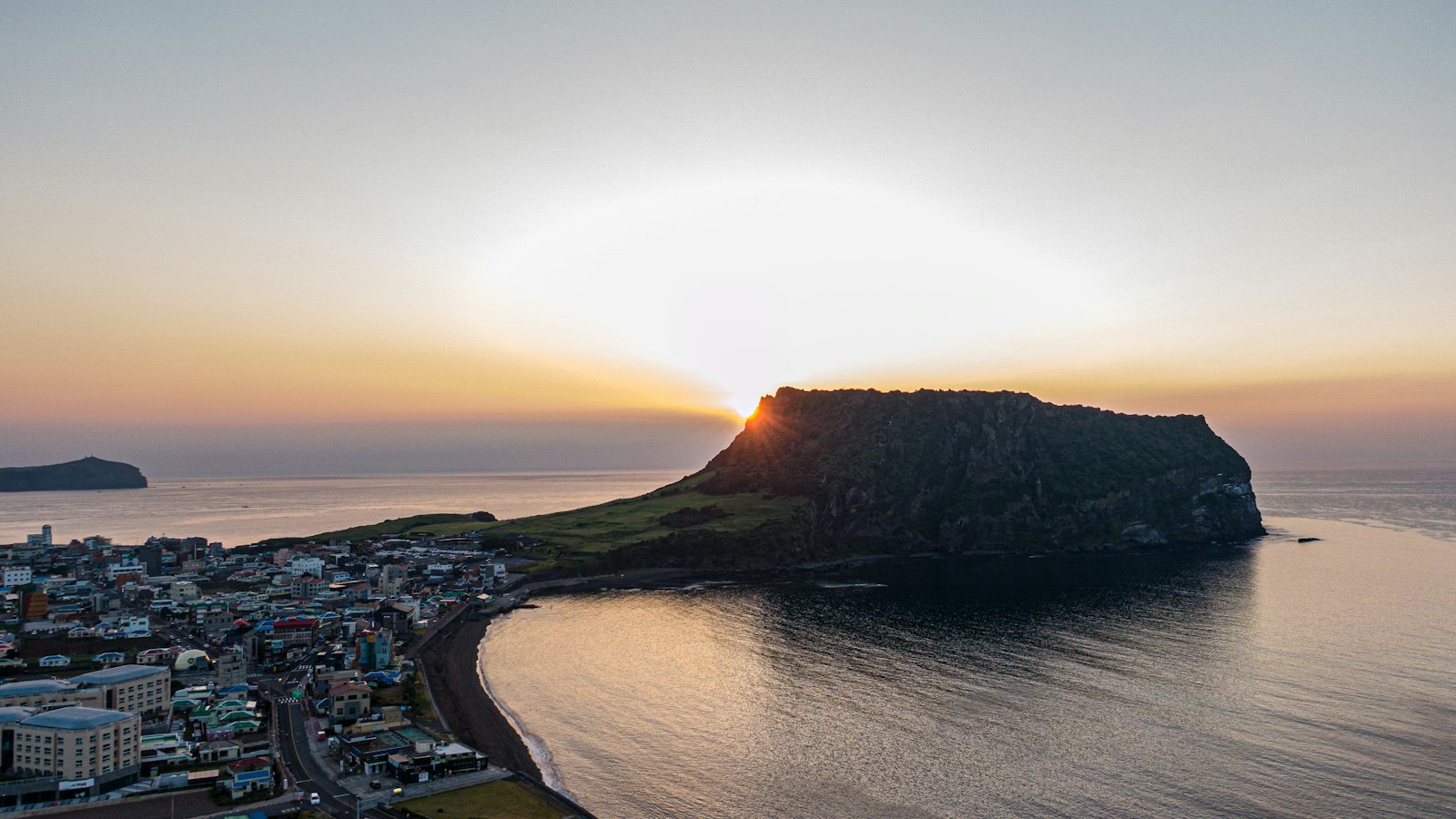 Sunrise bursting over Seongsan Ilchulbong crater above Seongsan town and bay, Jeju Island
