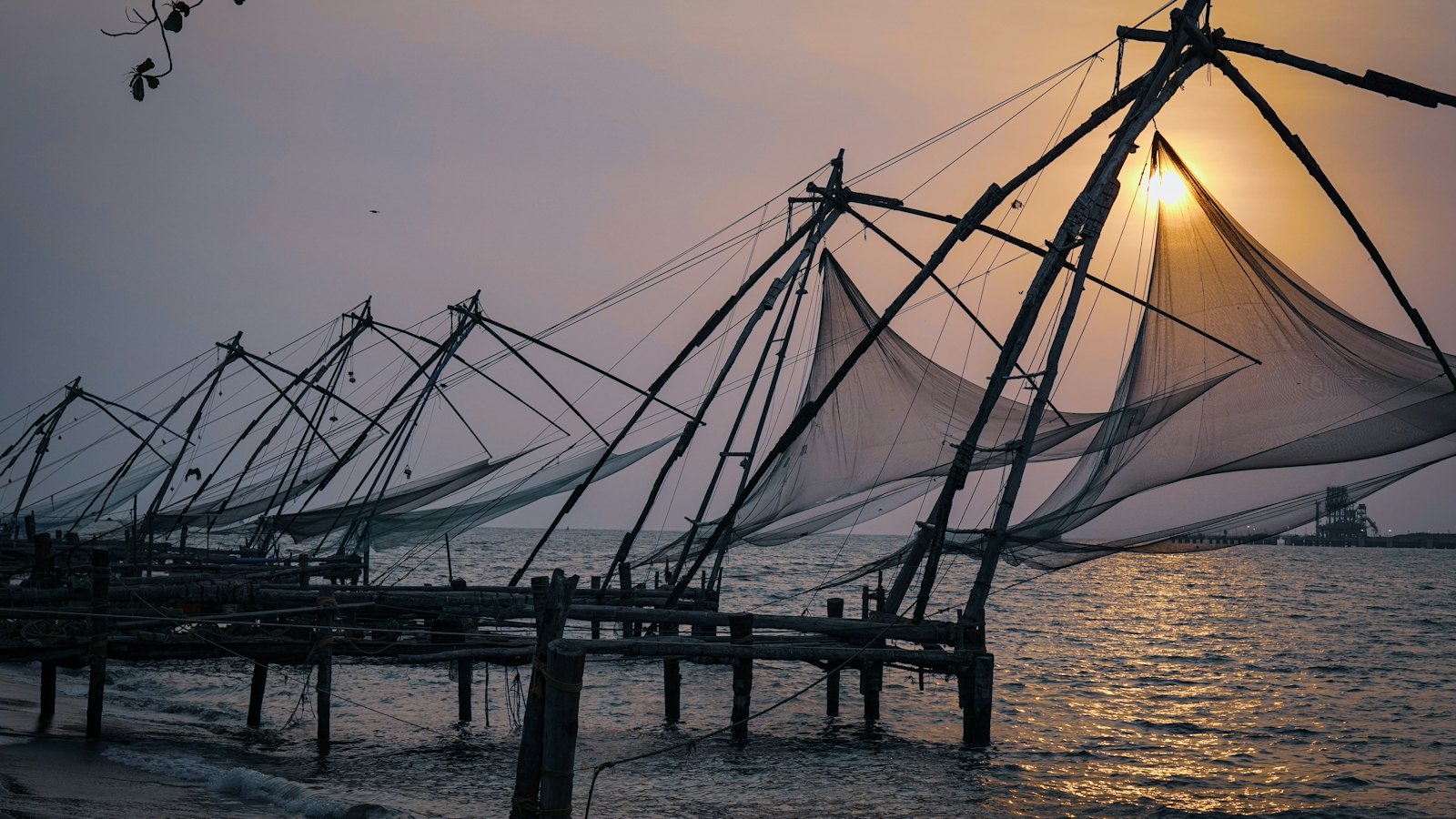 Row of Chinese fishing nets silhouetted against the setting sun on the shore of Fort Kochi, Kerala