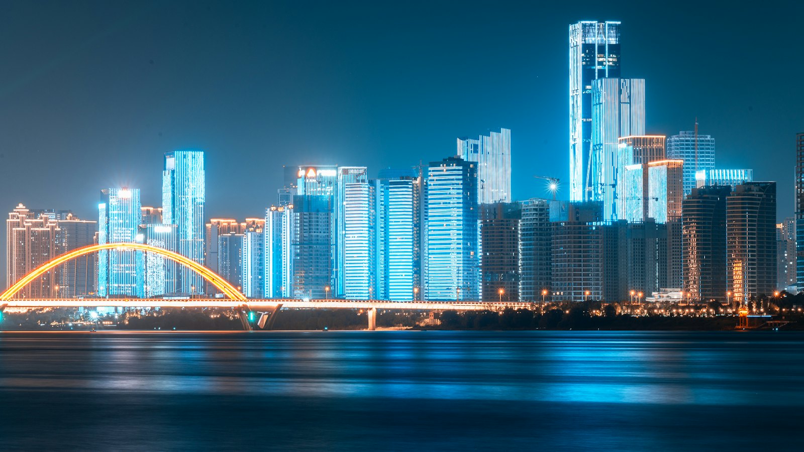 An arched bridge glows orange beneath Changsha's blue-lit night skyline