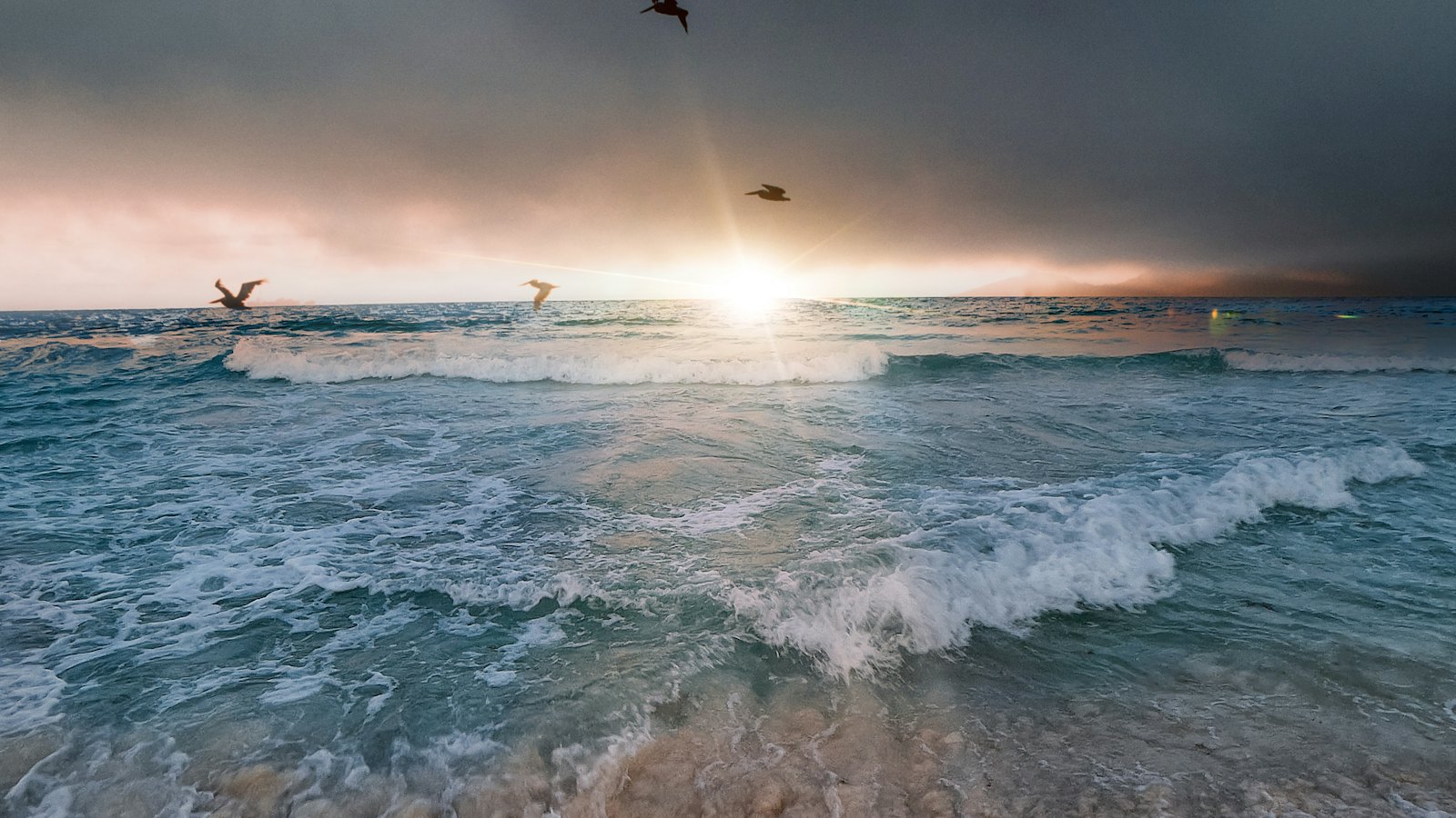 Waves rolling onto a Cancun beach as the sun sets through stormy skies