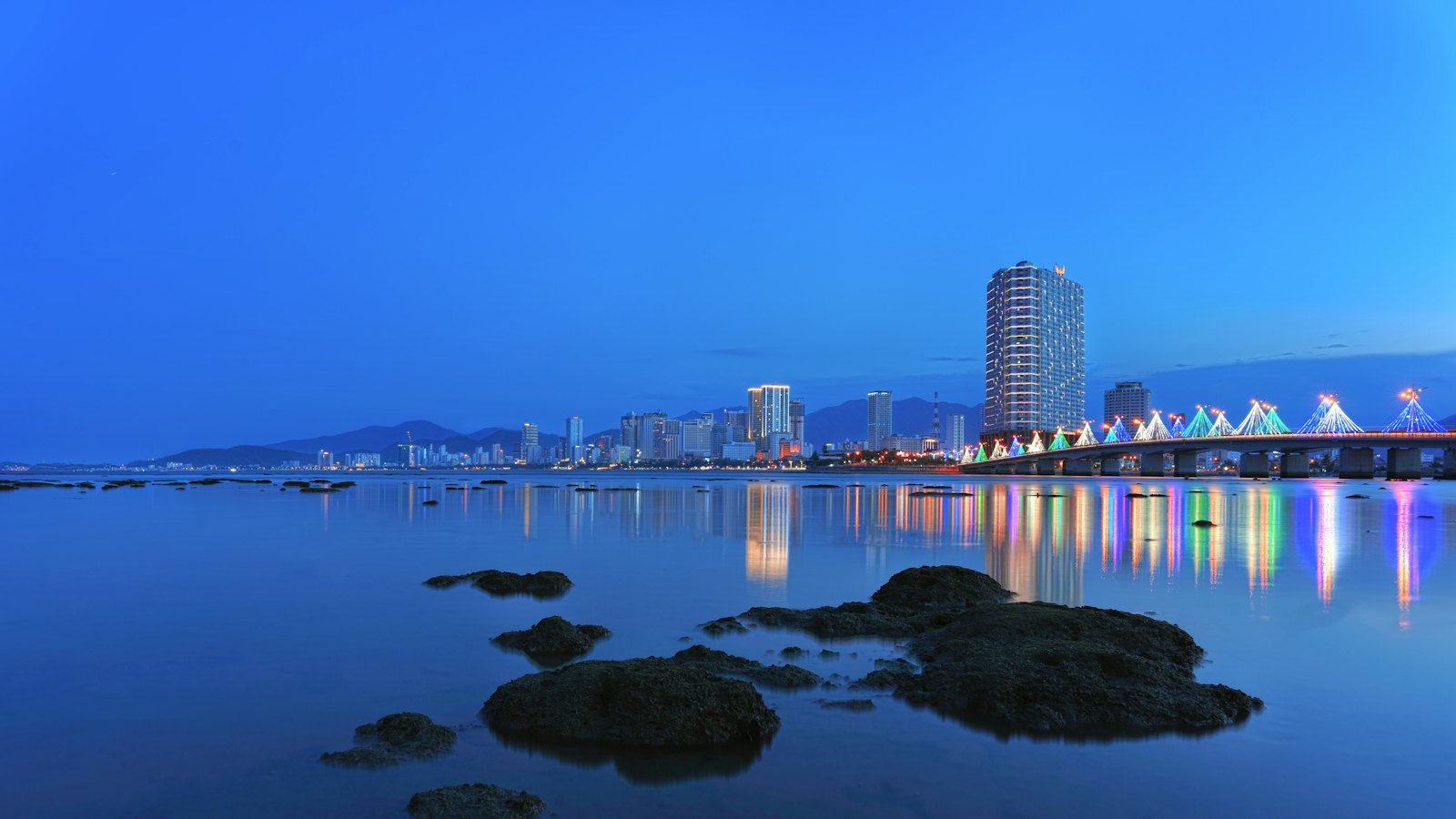 Tran Phu Bridge and Nha Trang skyline lit at blue hour, reflected in calm water
