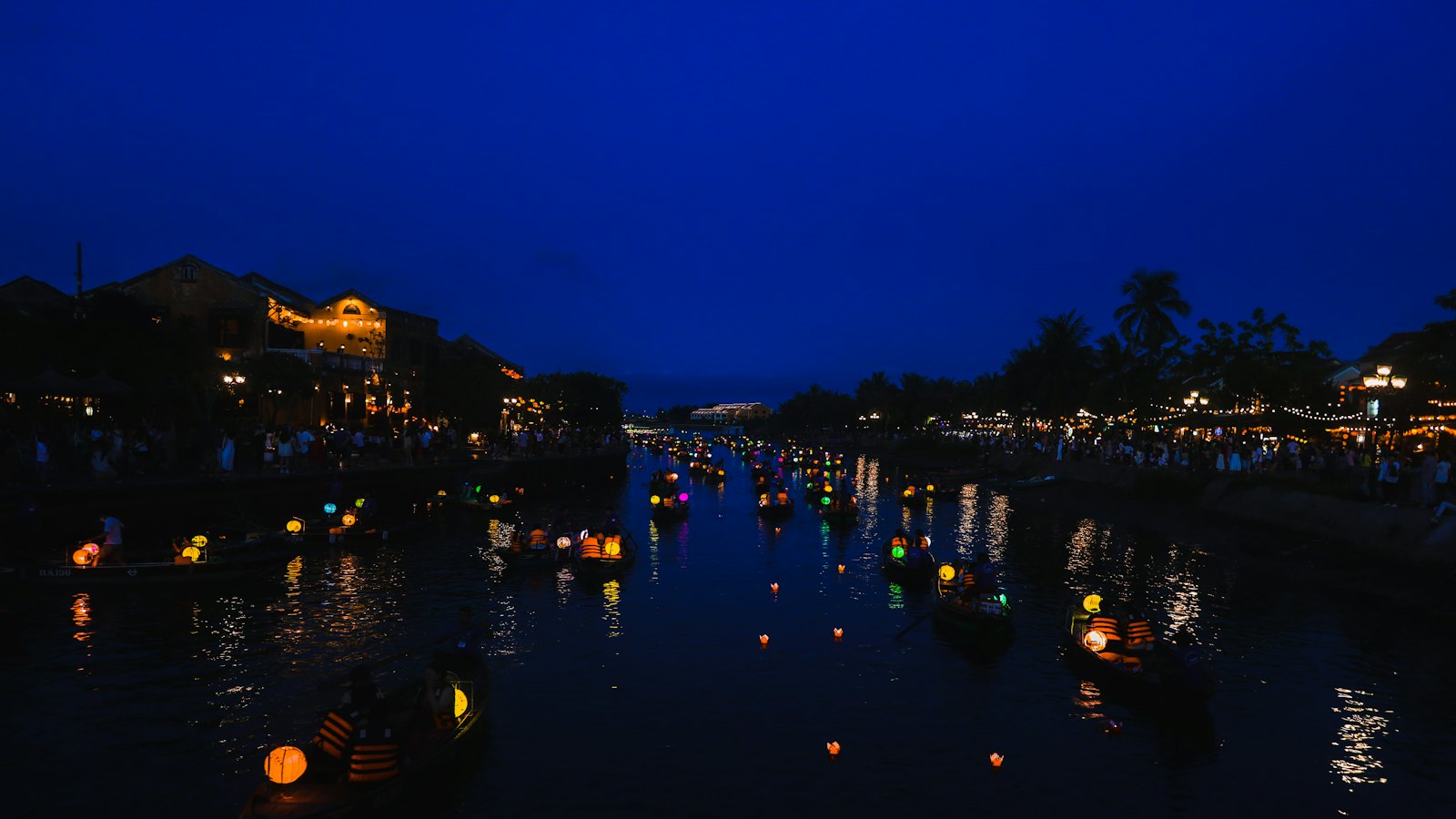 Floating paper lanterns glow on Hoi An's river at blue hour