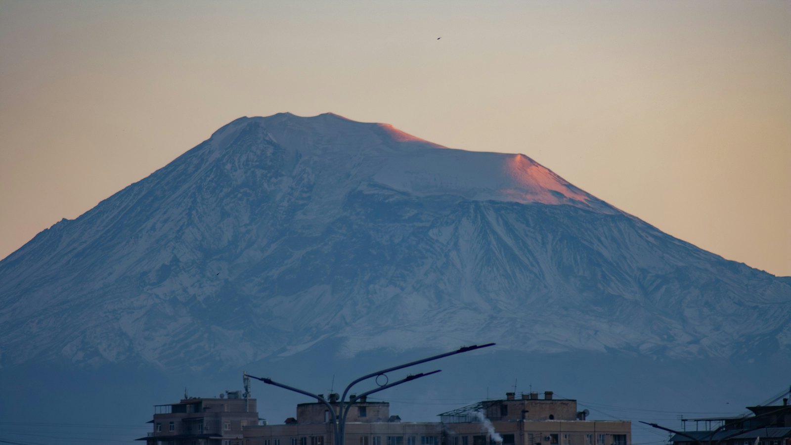 Snow-capped Mount Ararat glowing at sunset above the rooftops of Yerevan