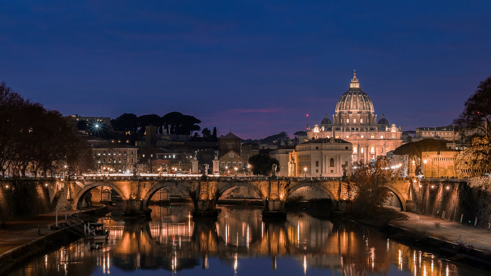 St. Peter's dome glows above Ponte Sant'Angelo and the Tiber in Rome at blue hour