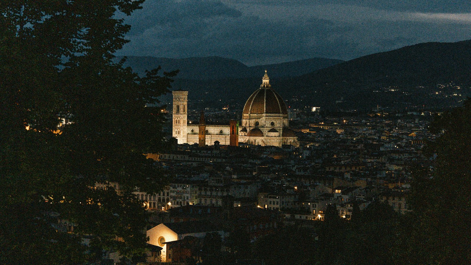 The Duomo's illuminated dome rising above Florence's rooftops at twilight