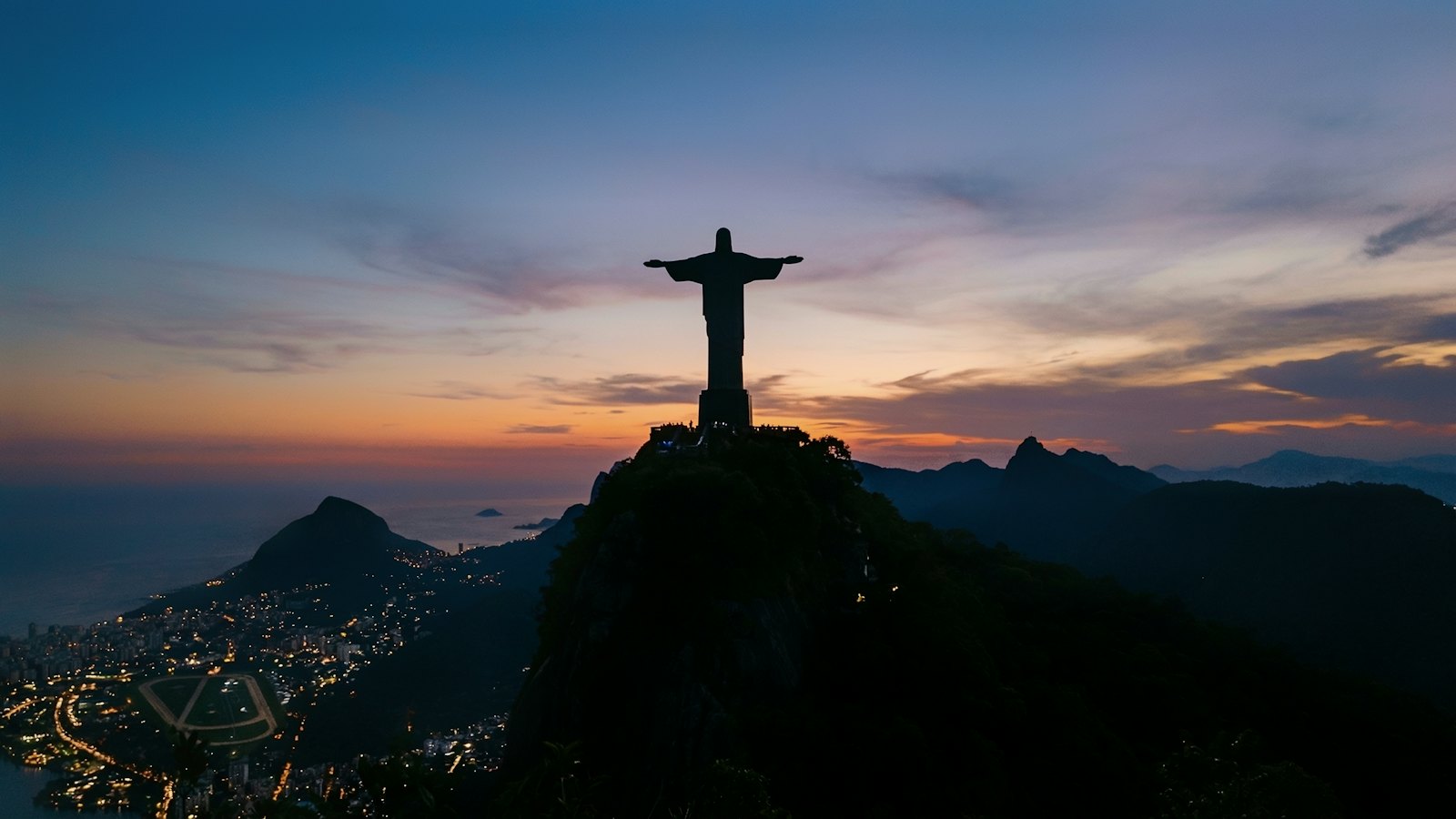 Christ the Redeemer statue silhouetted at dusk above Rio de Janeiro's city lights