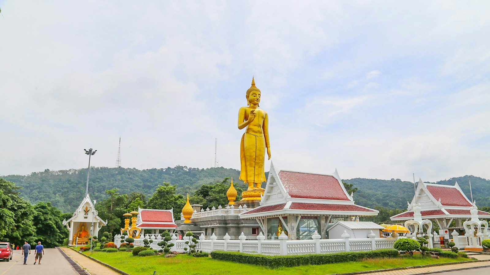 Giant golden standing Buddha statue rising above temple pavilions at Hat Yai Municipal Park