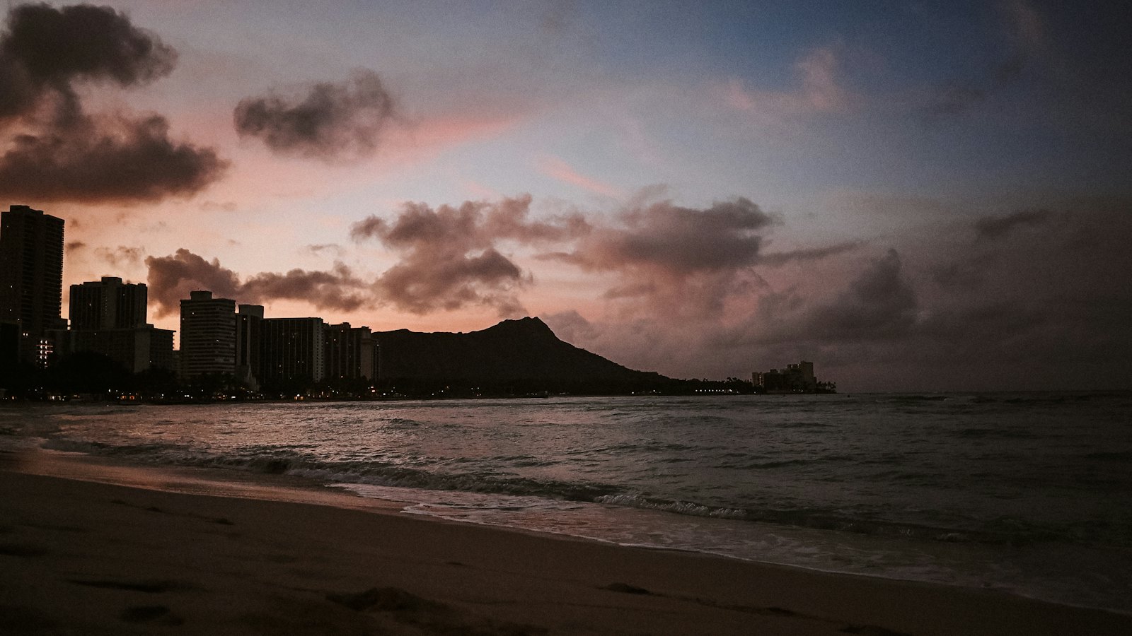Diamond Head crater silhouetted at dusk beside the lights of Waikiki Beach