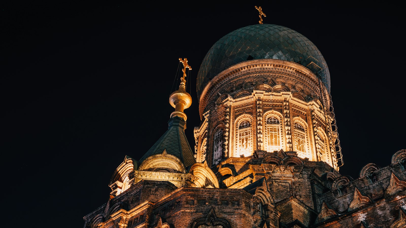 Saint Sophia Cathedral's green onion dome lit gold against the night sky in Harbin