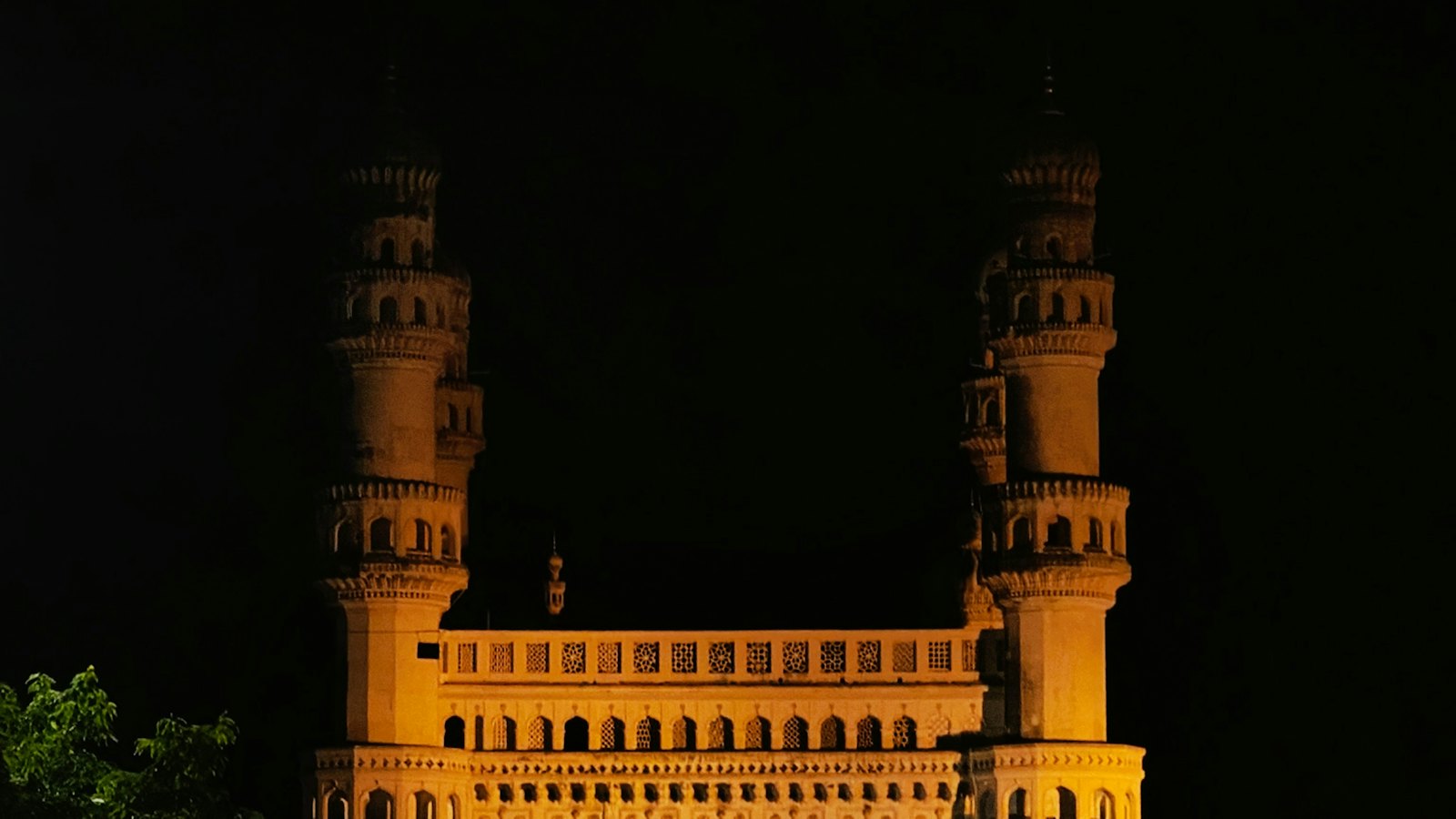 Charminar's four minarets glowing gold against the night sky in Hyderabad