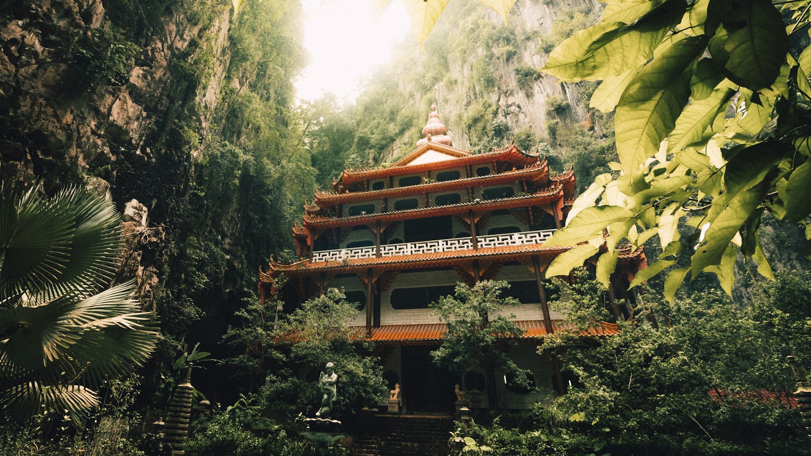 Multi-tiered Chinese cave temple beneath towering limestone cliffs and jungle foliage in Ipoh, Malaysia