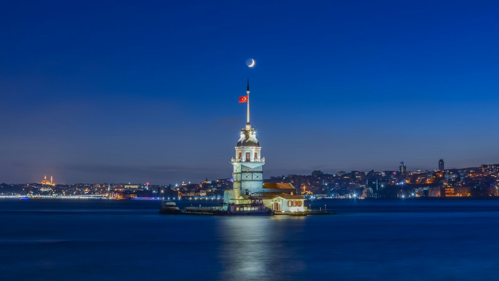 Maiden's Tower lit up on the Bosphorus at blue hour under a crescent moon, Istanbul