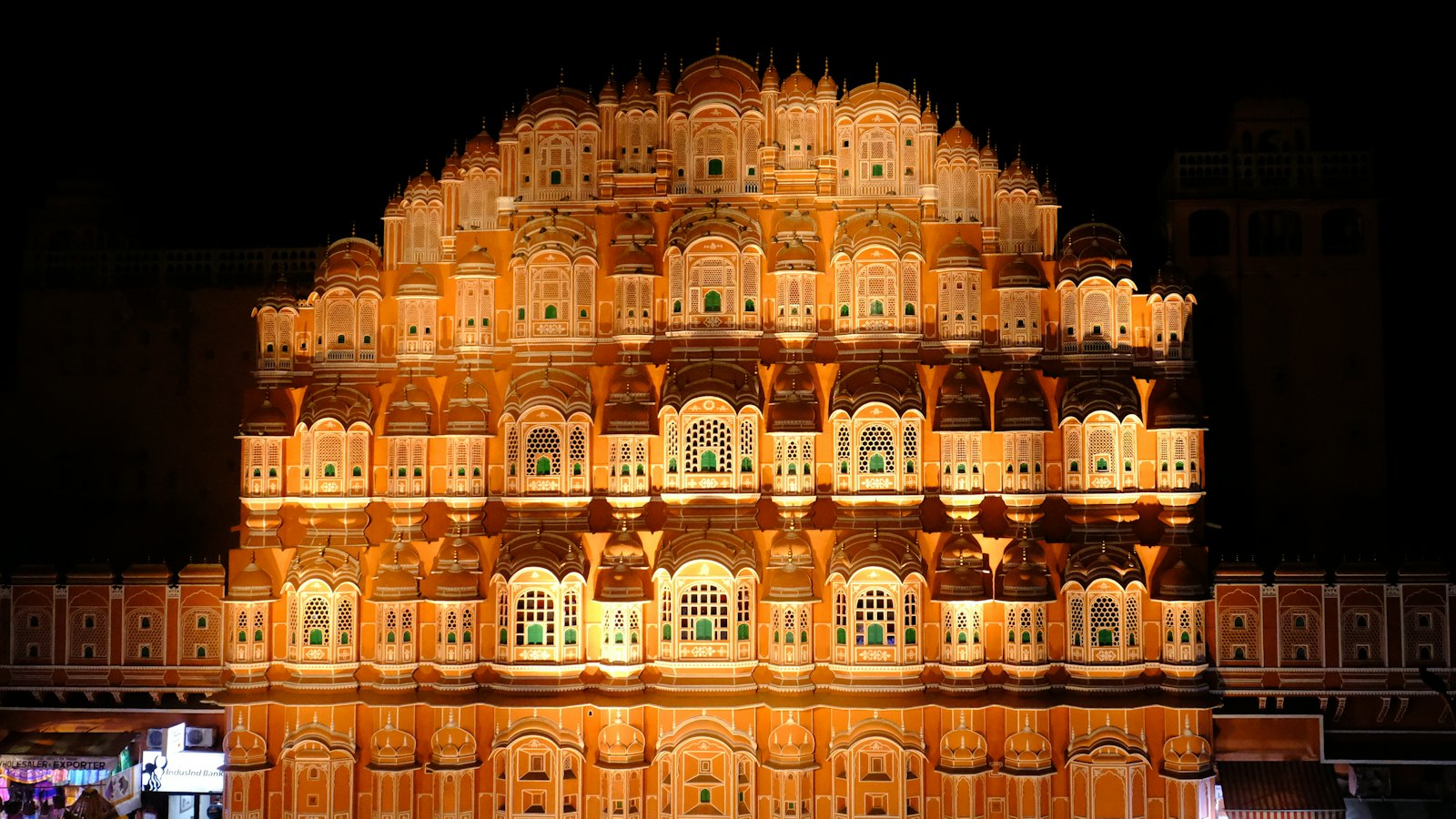 The illuminated pink sandstone facade of Hawa Mahal glowing against a black night sky in Jaipur