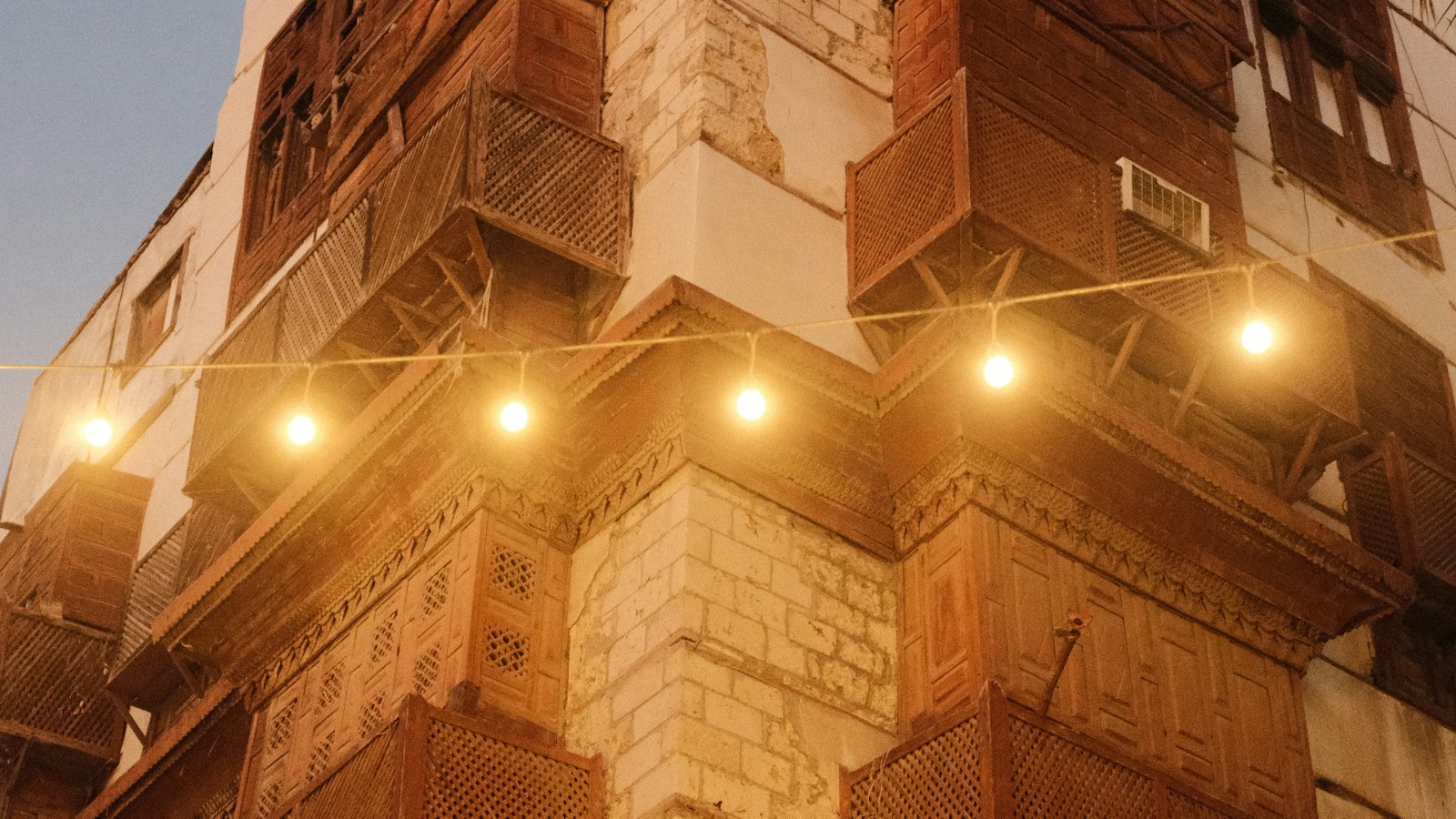 Coral-stone house with carved wooden rawasheen balconies and string lights at dusk in Al-Balad, Jeddah
