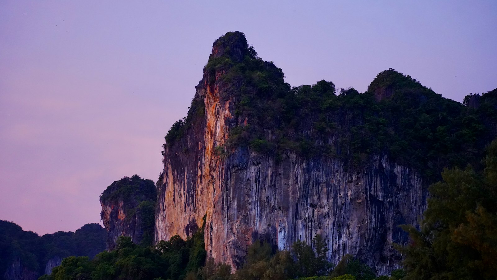 Towering limestone cliffs of Railay near Ao Nang, Krabi, glowing under a violet dusk sky