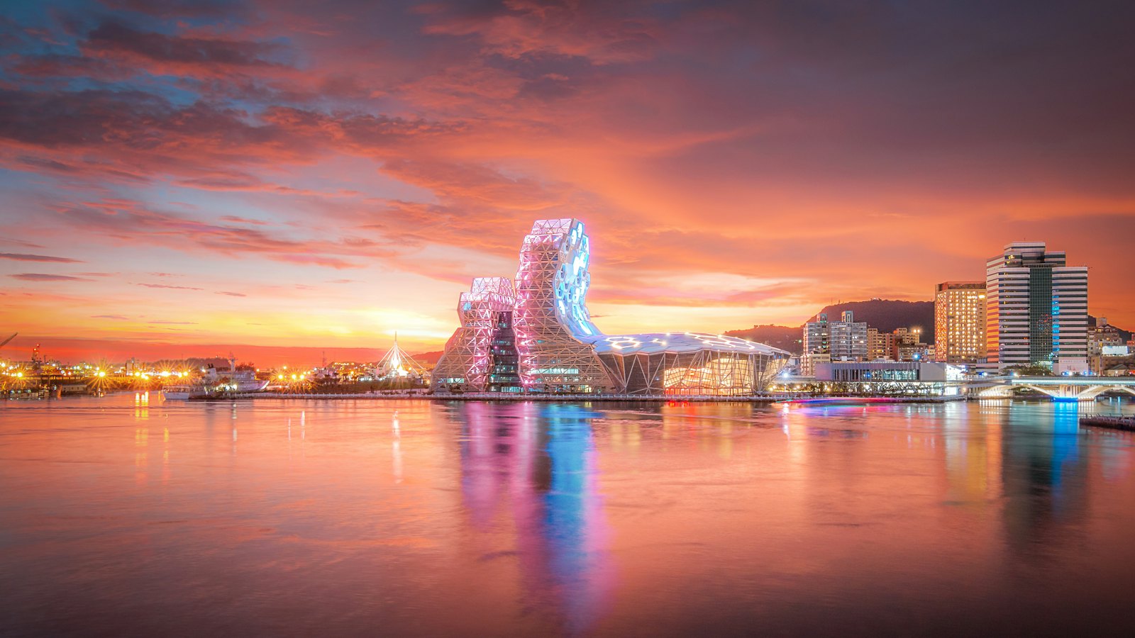 Kaohsiung Music Center glowing pink and blue over Kaohsiung Harbor at a fiery sunset