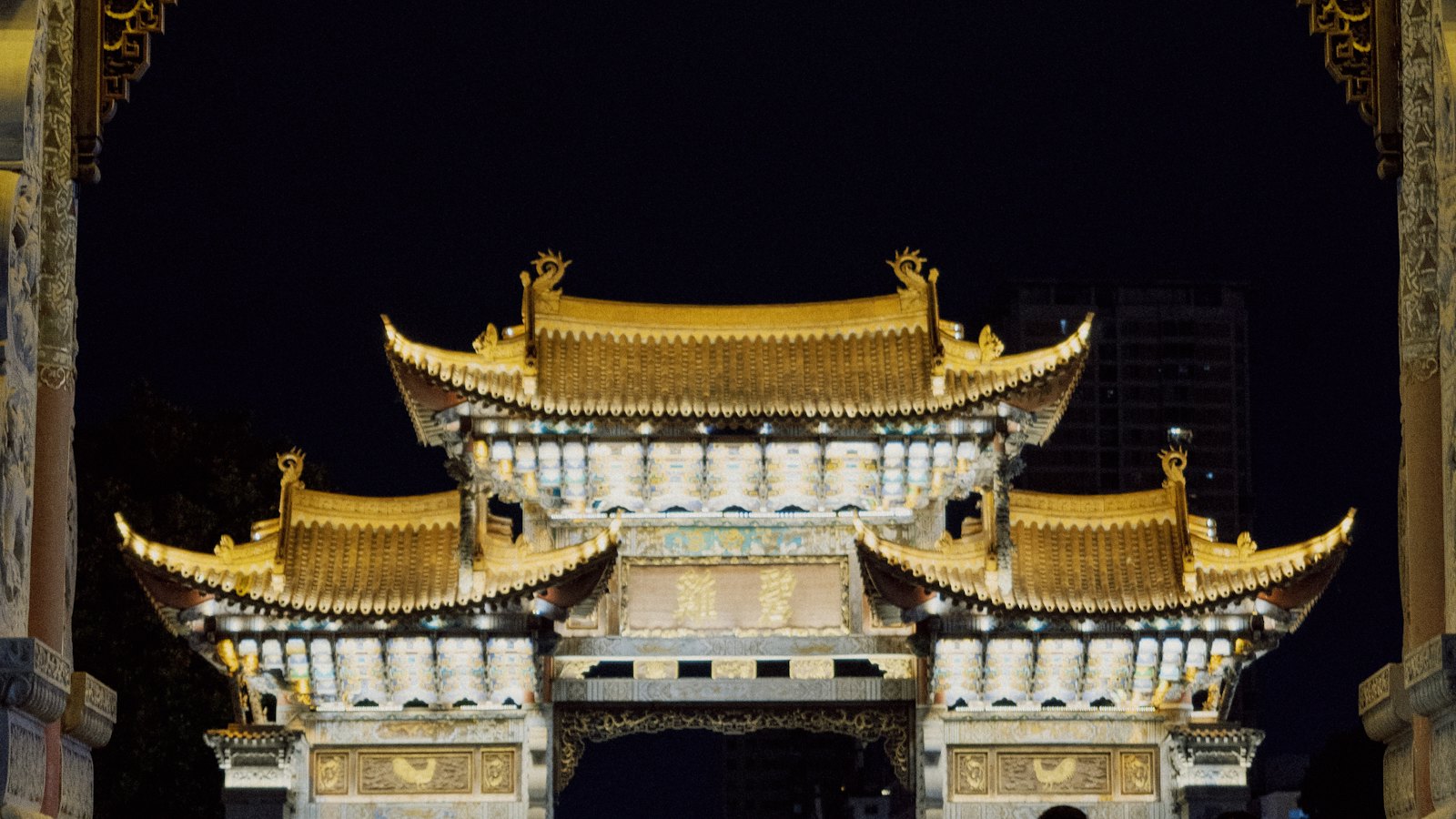 Golden Horse and Jade Rooster archways glowing gold against the night sky in Kunming, Yunnan