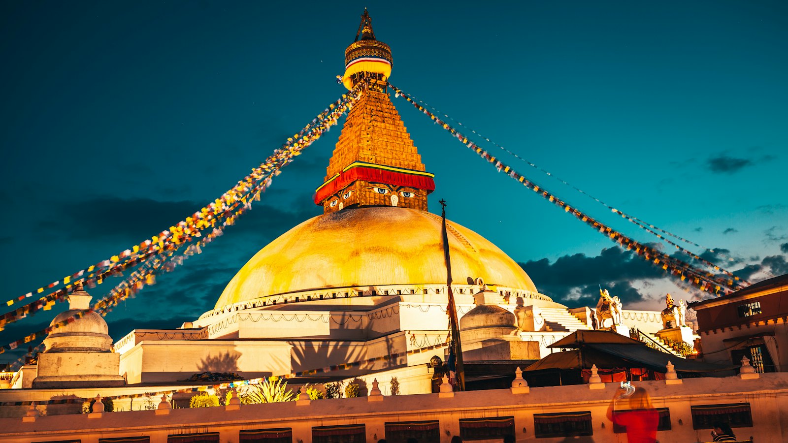 Boudhanath Stupa in Kathmandu glowing gold at blue hour, prayer flags against a teal sky