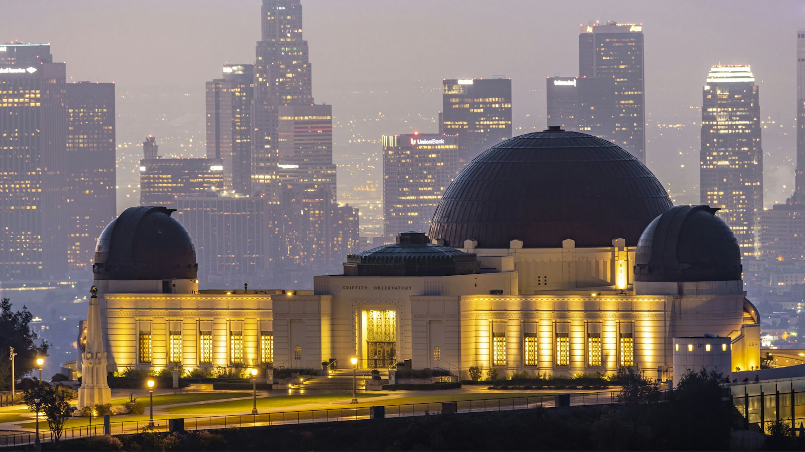 Griffith Observatory glowing at dusk with the downtown Los Angeles skyline rising behind it