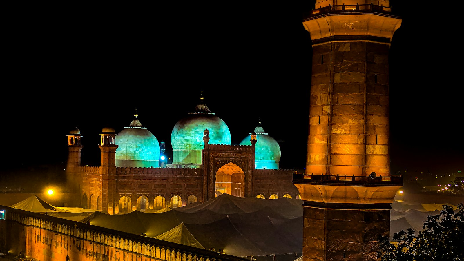 Badshahi Mosque's teal-lit domes and minaret glowing at night in Lahore