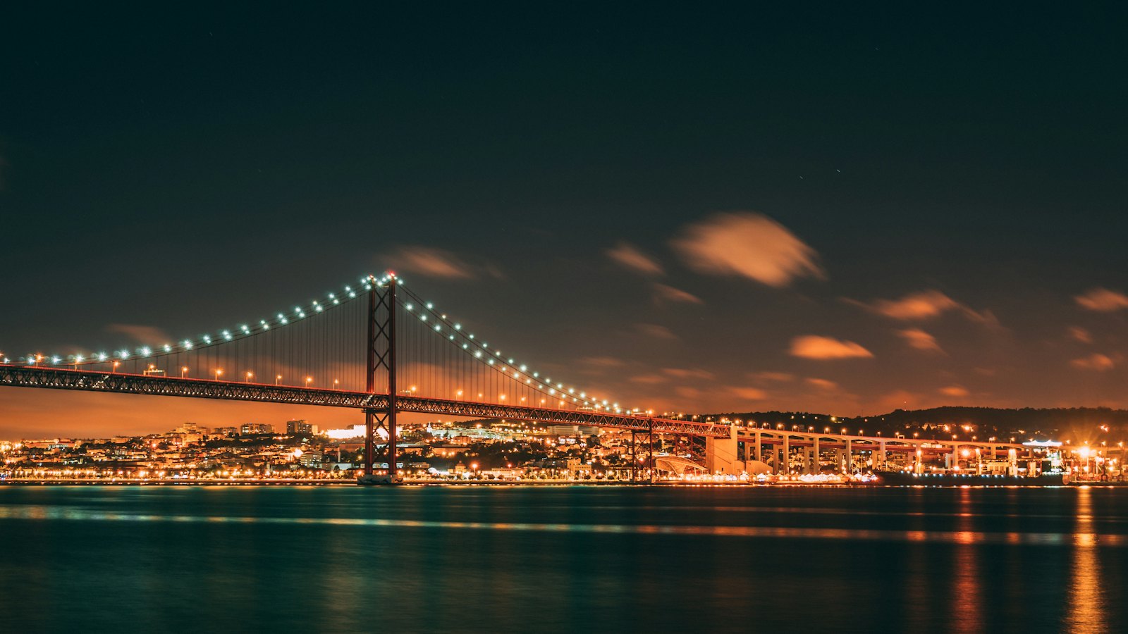 The 25 de Abril suspension bridge illuminated at night over the Tagus in Lisbon