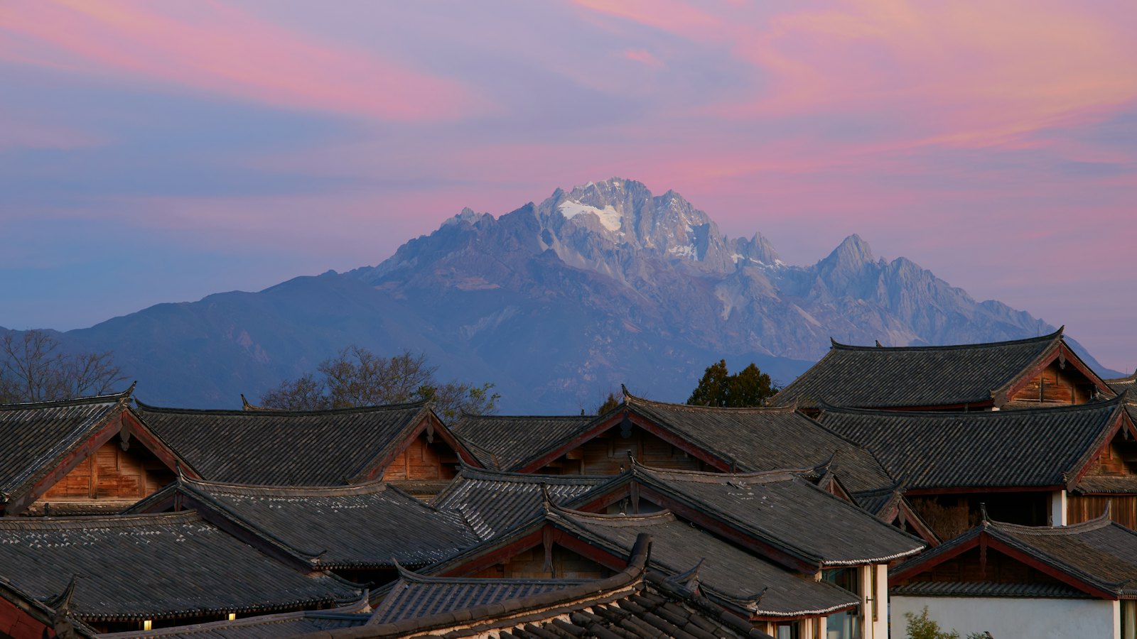 Snow-capped Jade Dragon Snow Mountain rising above Lijiang Old Town's rooftops at dusk