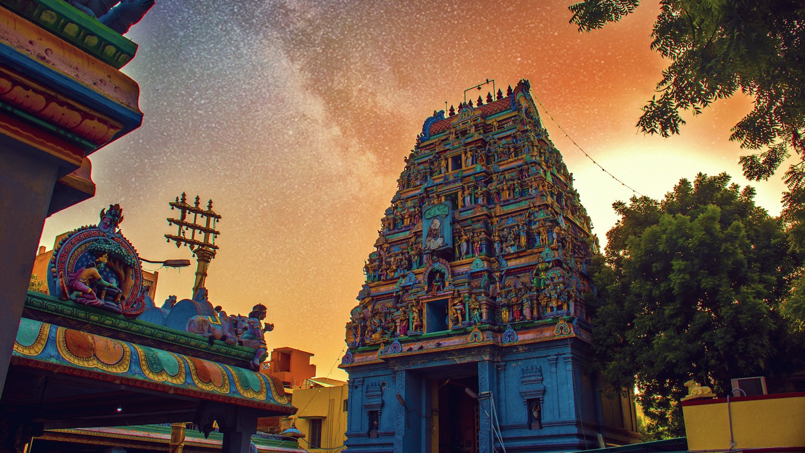 Painted Dravidian temple gopuram in Chennai rising beneath a starry night sky with warm glow
