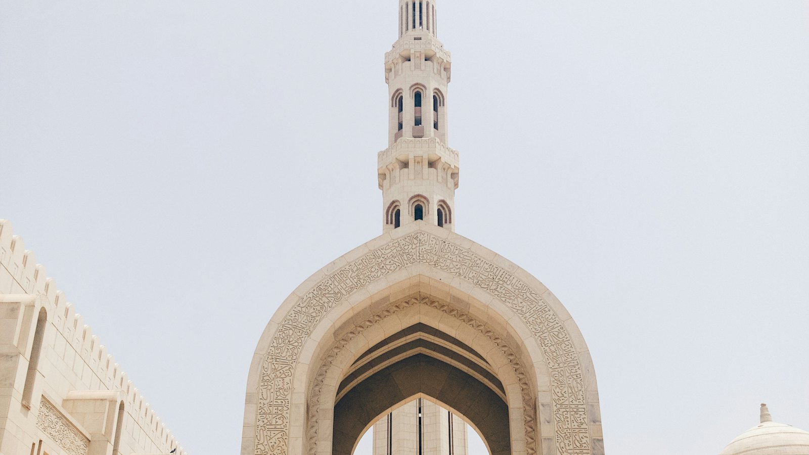 Sultan Qaboos Grand Mosque's minaret framed by a carved stone archway in Muscat