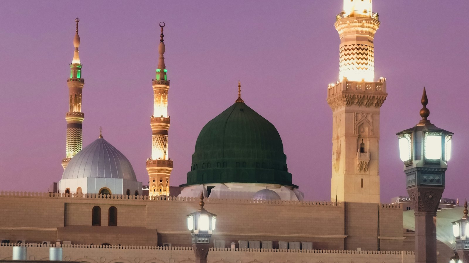 The Green Dome and lit minarets of the Prophet's Mosque in Madinah under a violet dusk sky