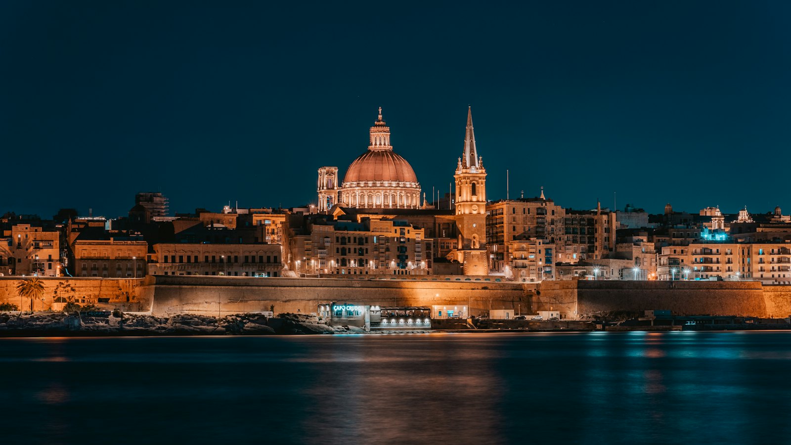 The domed Carmelite Church and Valletta skyline glowing at night across the harbour