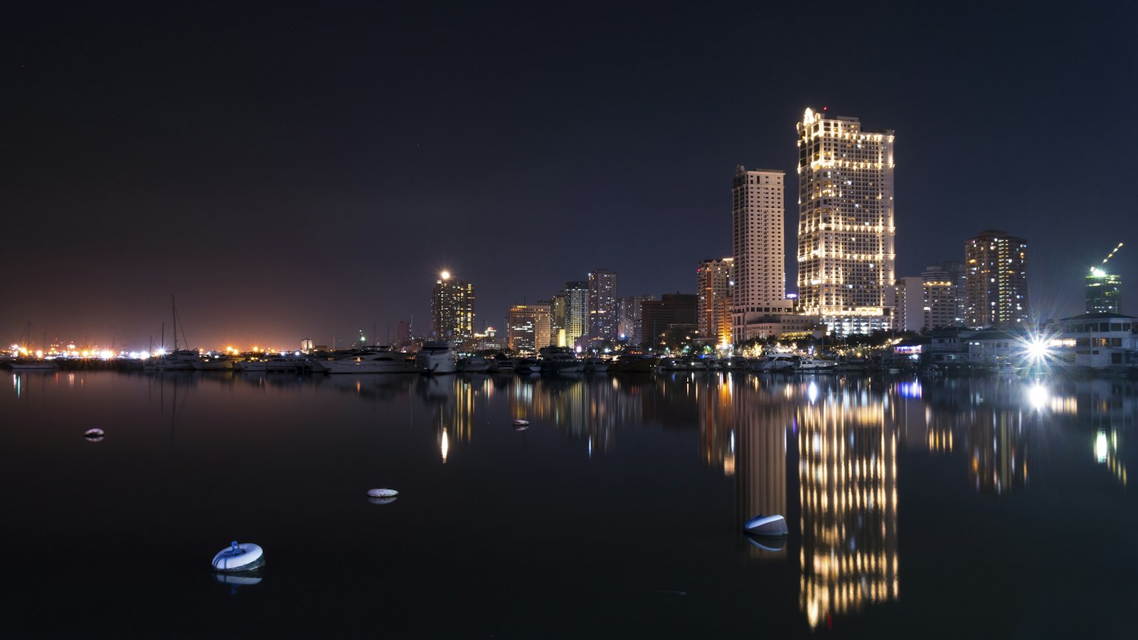 Manila Bay skyline at night, lit towers mirrored in the still marina water