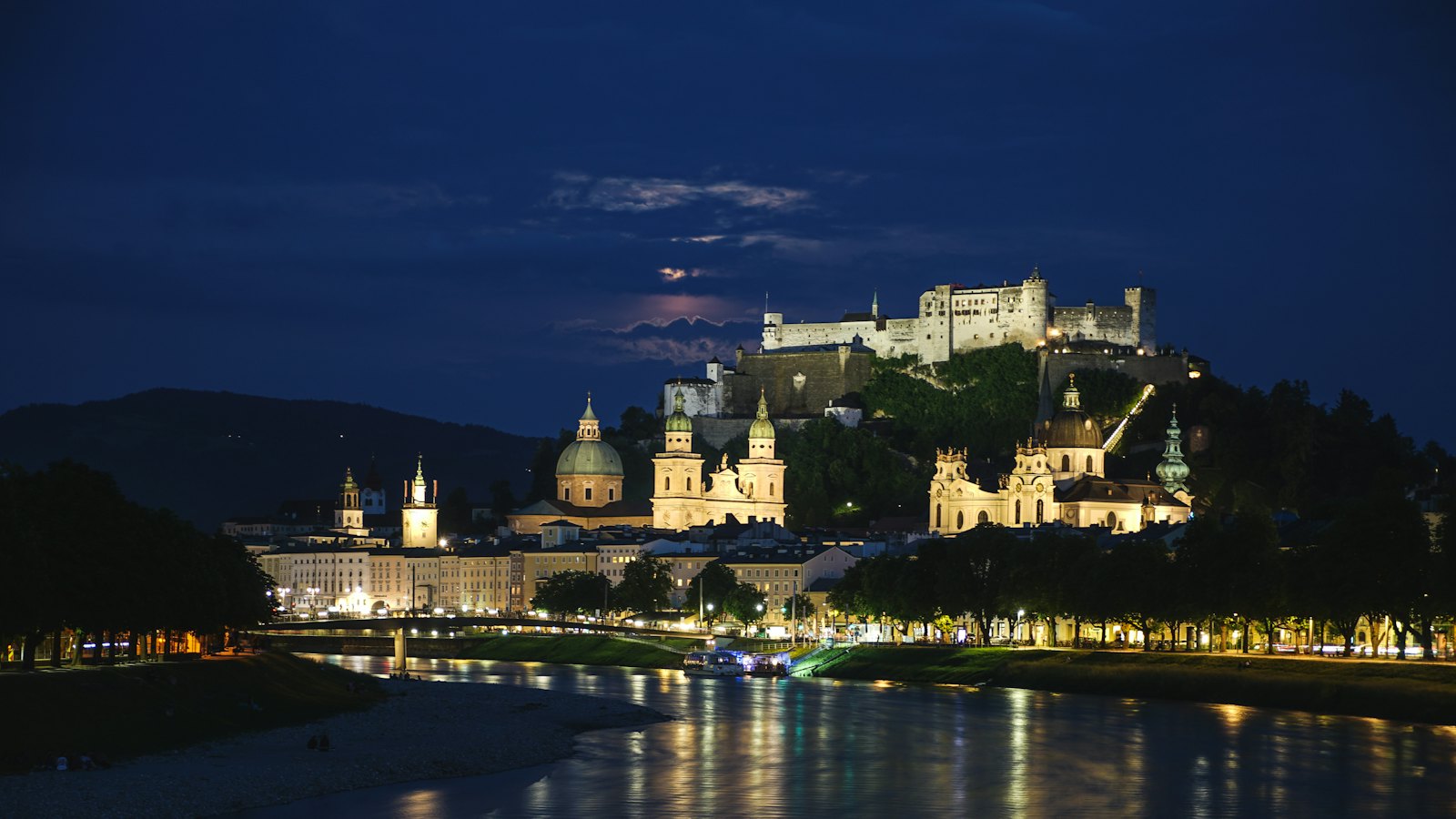 Hohensalzburg Fortress lit up above Salzburg's old town and the Salzach river at night