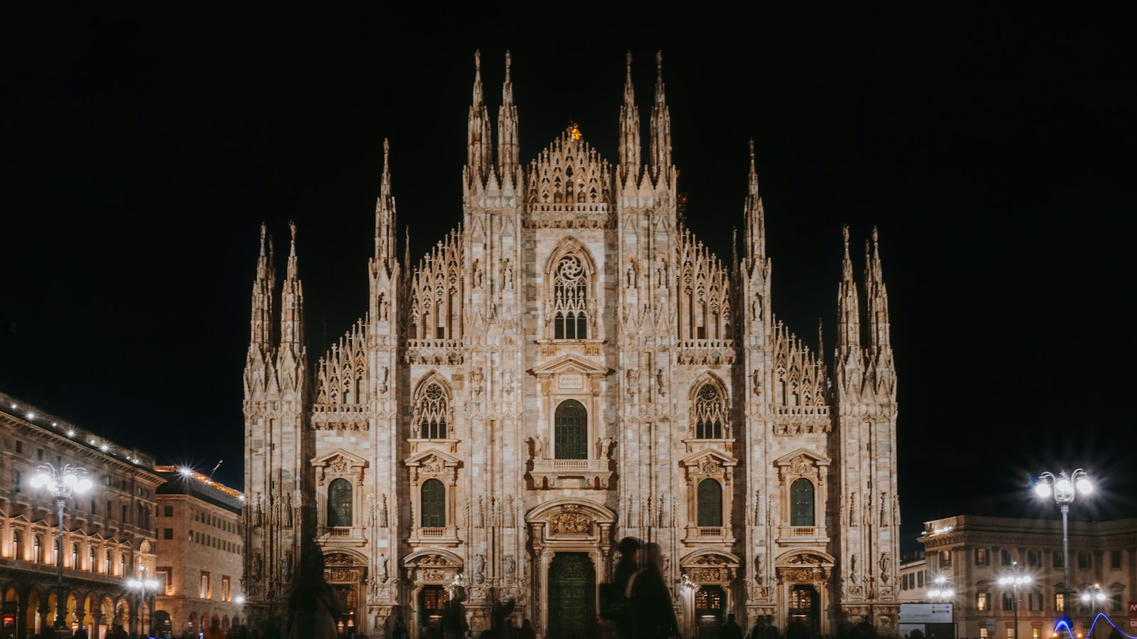 Milan Cathedral's marble Gothic facade glowing at night above Piazza del Duomo, Milan, Italy