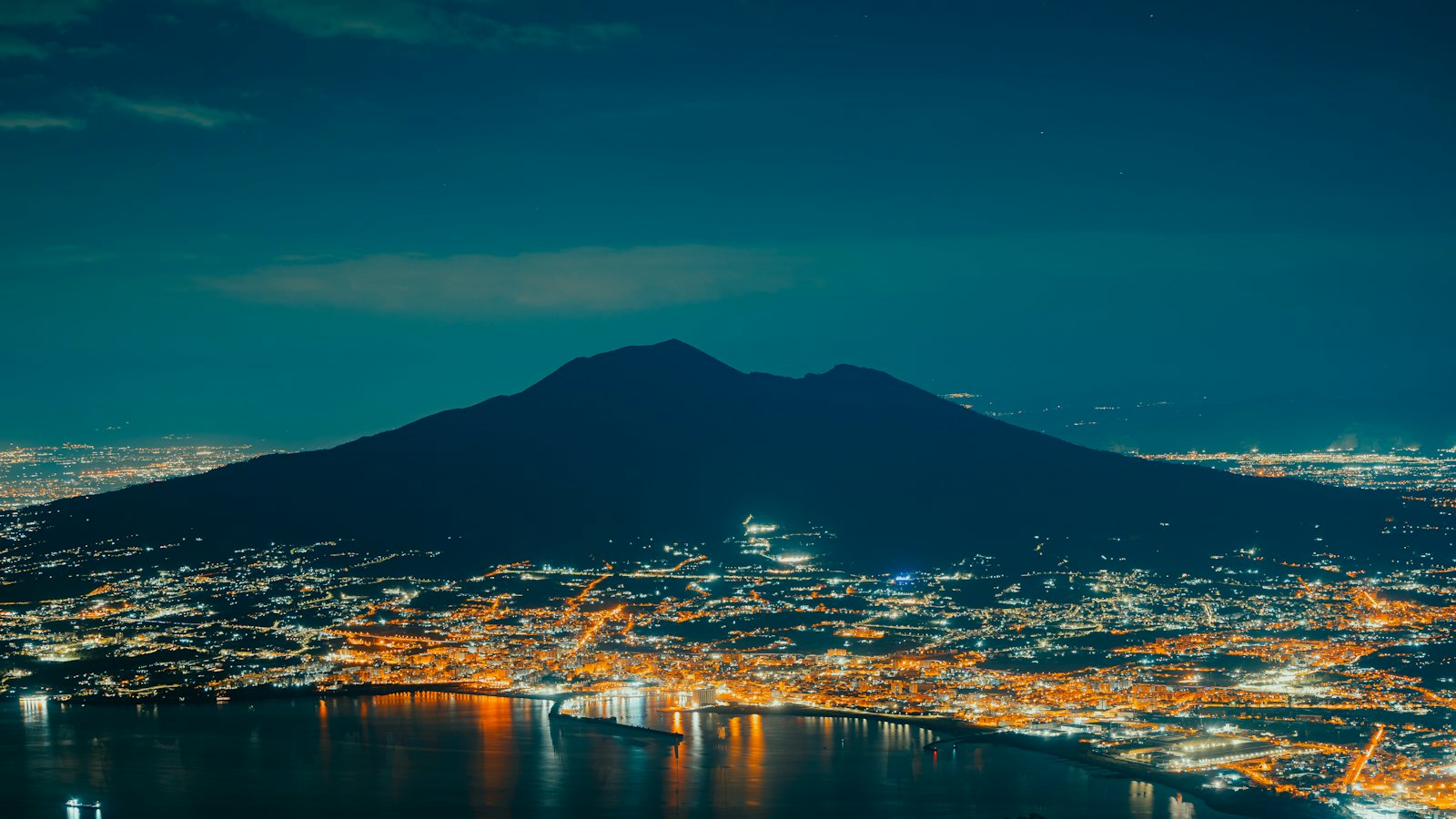 Mount Vesuvius silhouetted at night above the illuminated Bay of Naples
