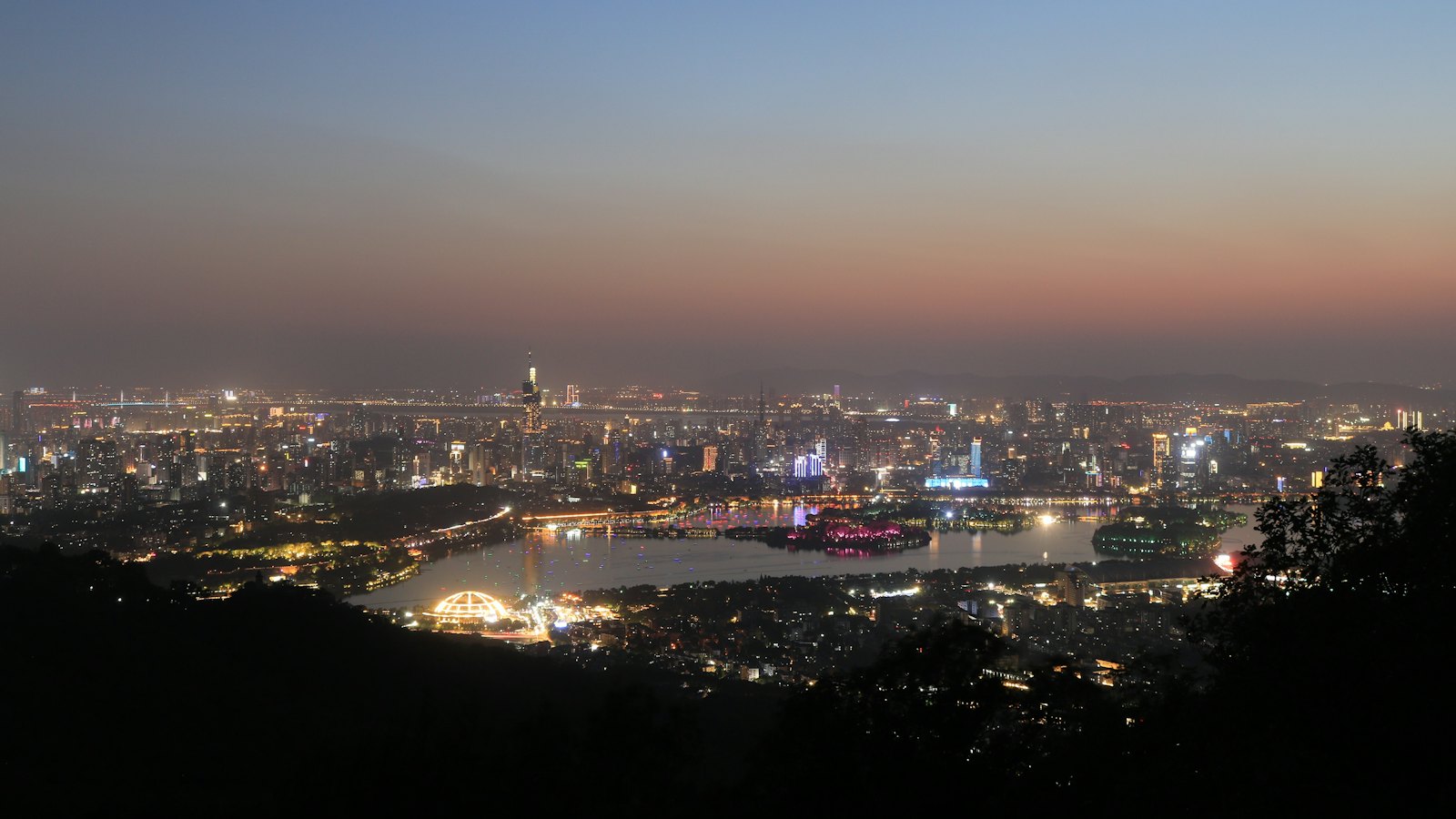 Nanjing's skyline glows at dusk along the river seen from a hilltop