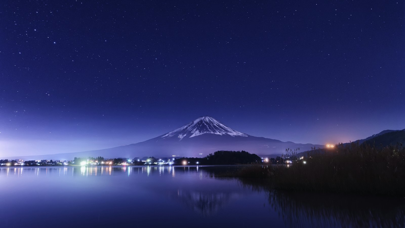 Mount Fuji's snow-capped peak reflected in Lake Kawaguchi under a starry night sky